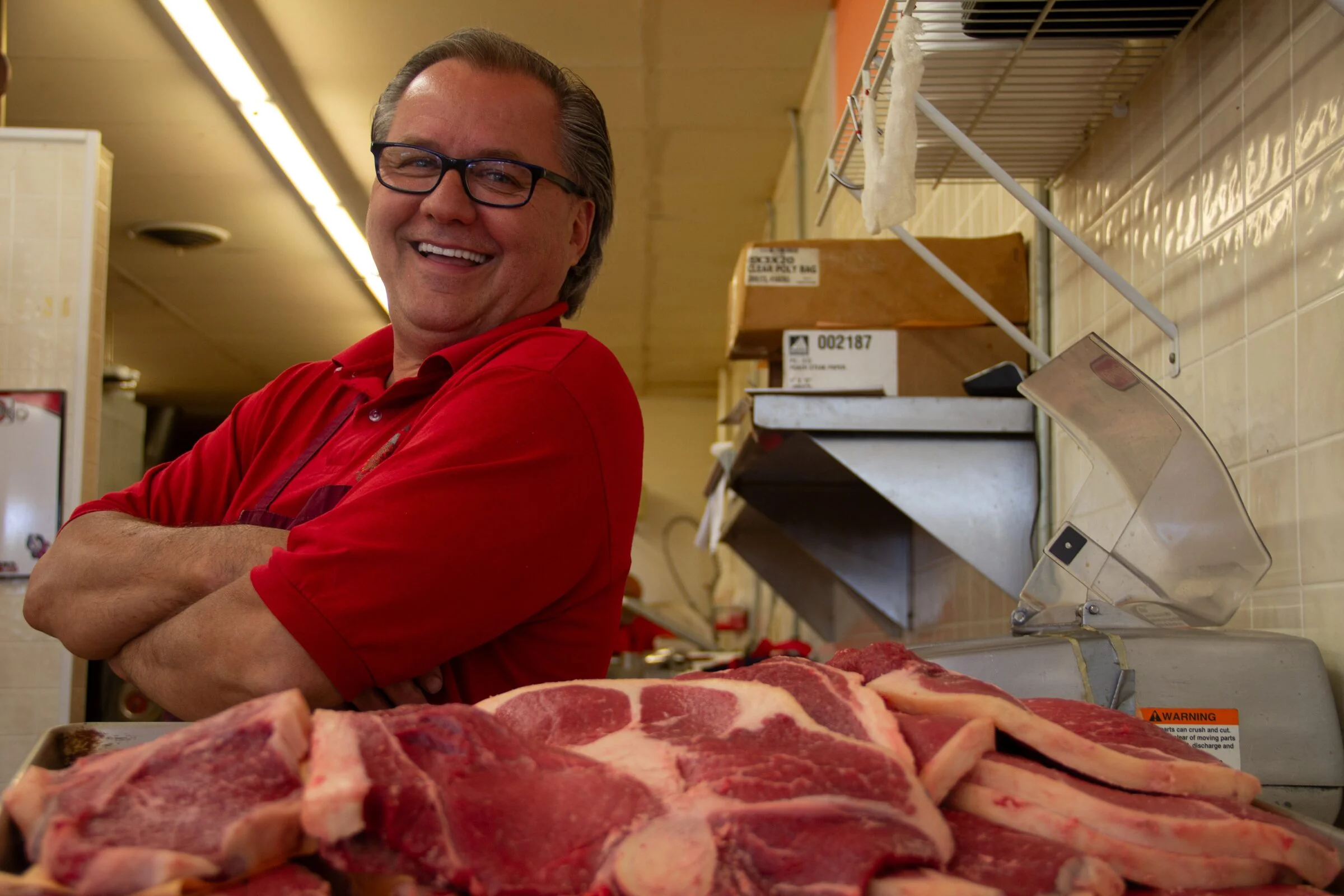 Mark Jaworski, the Kielbasa Kid, smiling behind the fresh meat counter at Jaworski Meats with ribeyes and chops on display